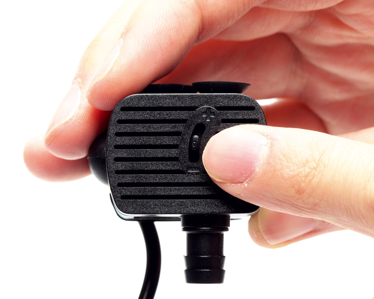 Das Bild zeigt eine kleine, schwarze Pumpe, die mit einem Finger an einem Drehregler bedient wird.